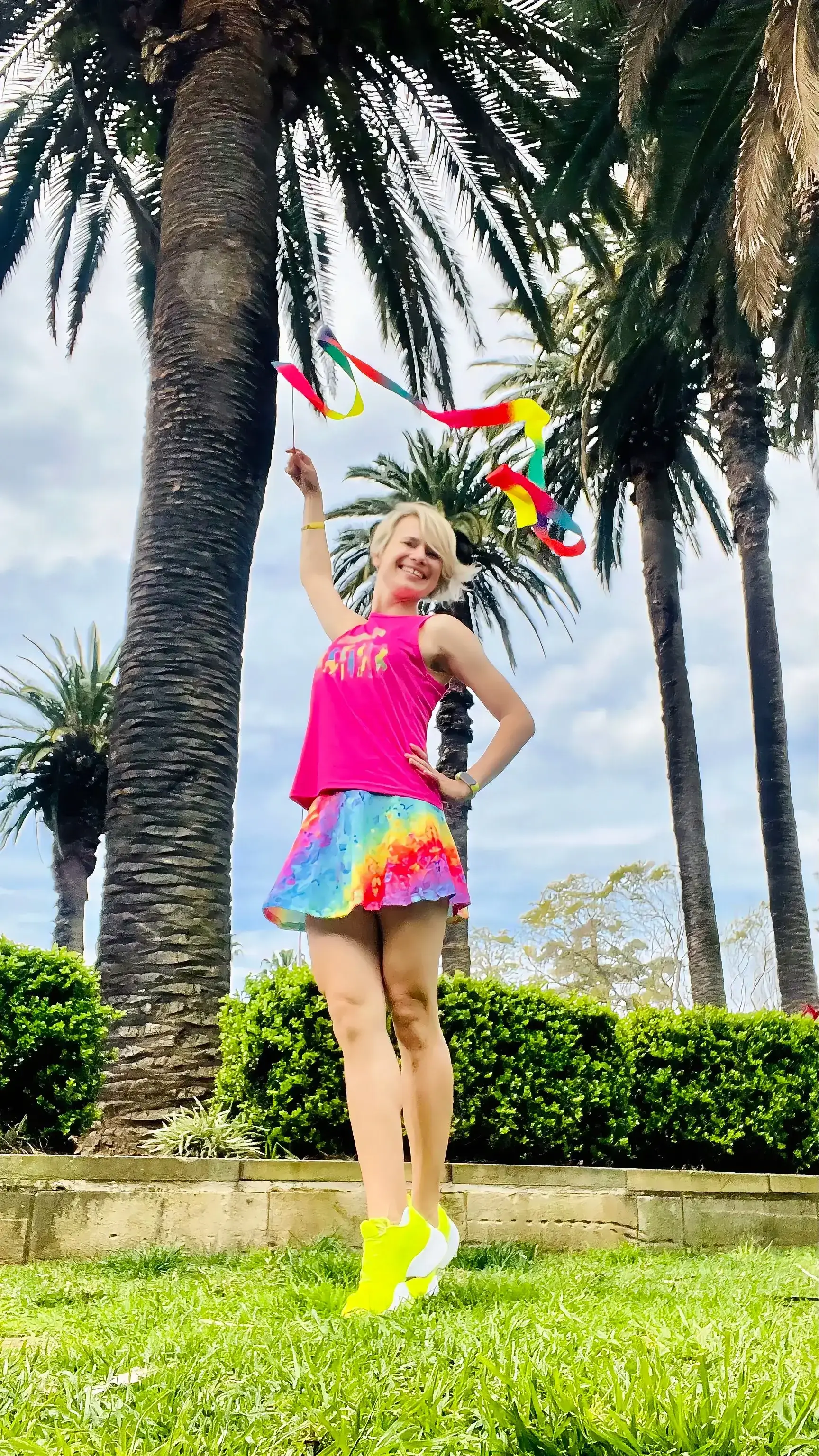 Elena spinning a rainbow gymnastics ribbon under palm trees