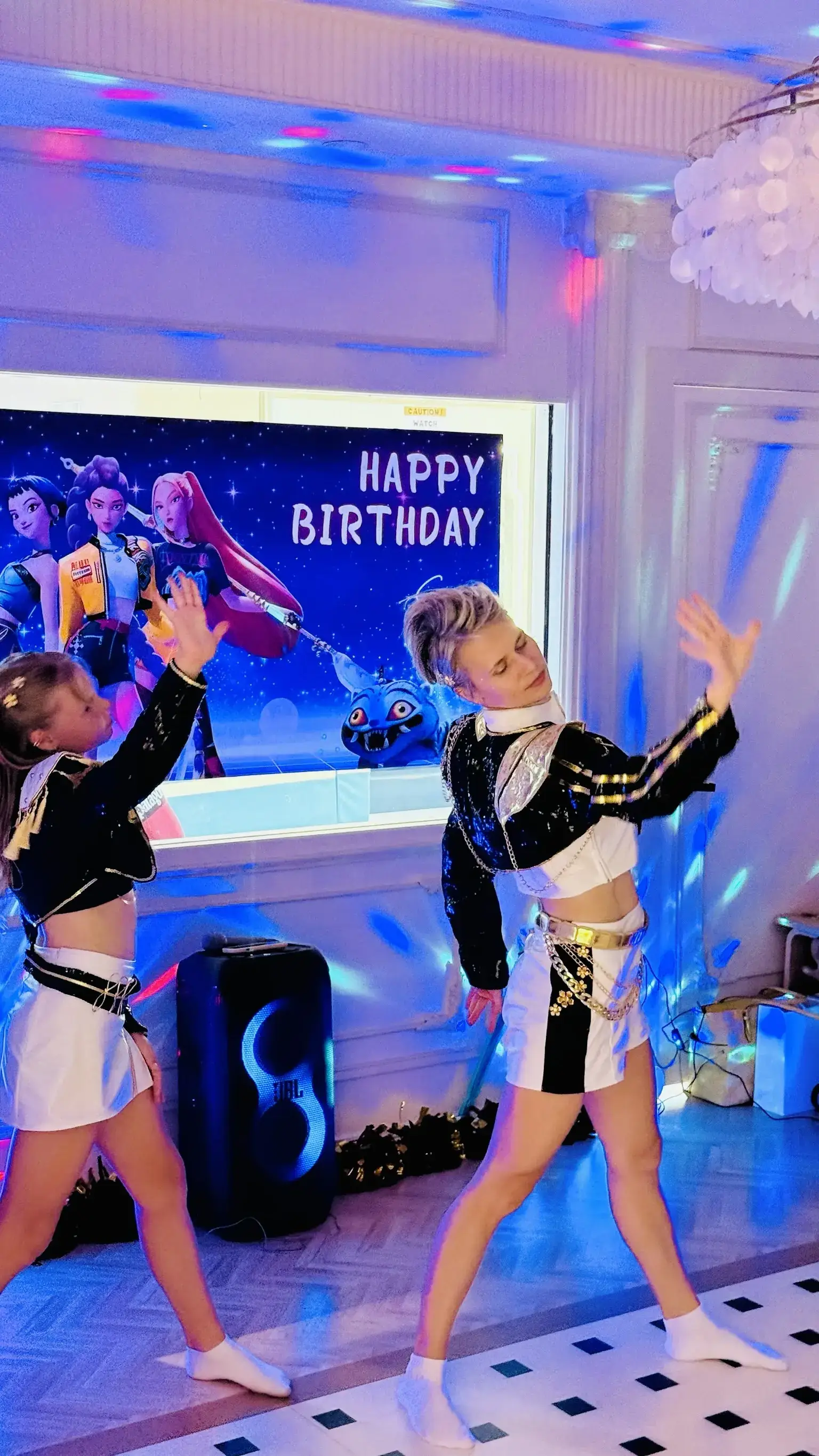 Professional dance party entertainer and child in Huntr/x costumes dancing in front of a Happy Birthday screen under disco lights