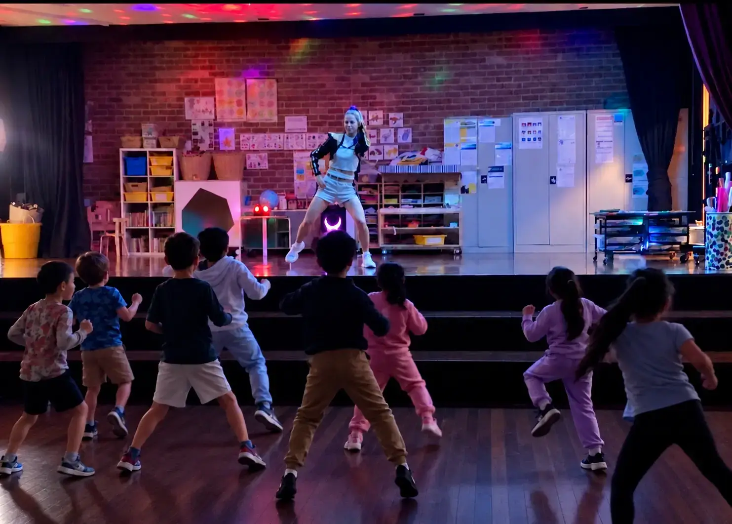 Professional dance party entertainer in K-Pop costume dancing on stage while a group of kids copies the routine