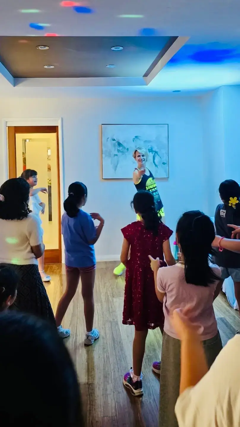 Kids following the professional dance party entertainer's moves in a living room lit by disco lights