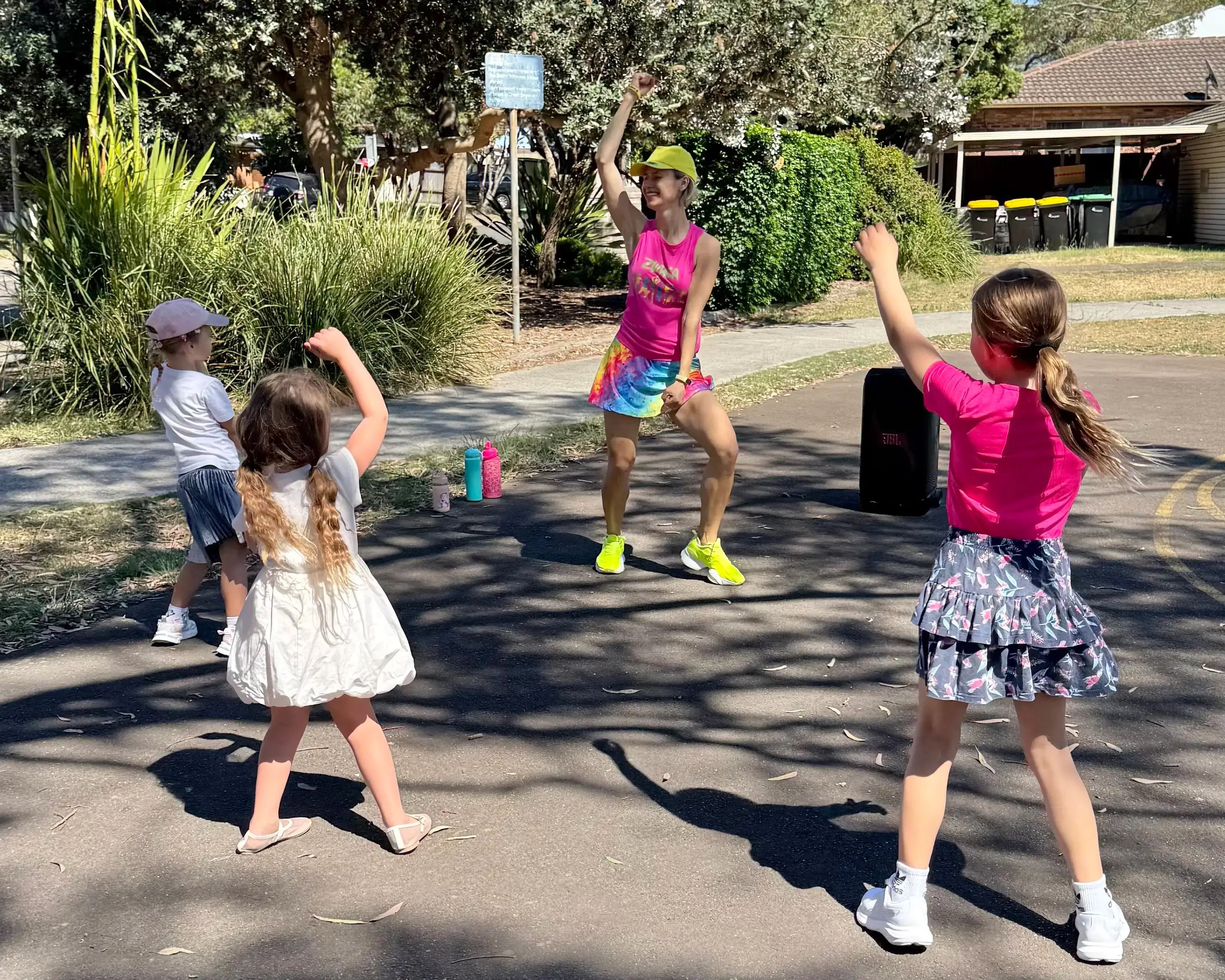 Professional dance party entertainer and three children dancing outdoors in the sun with a speaker