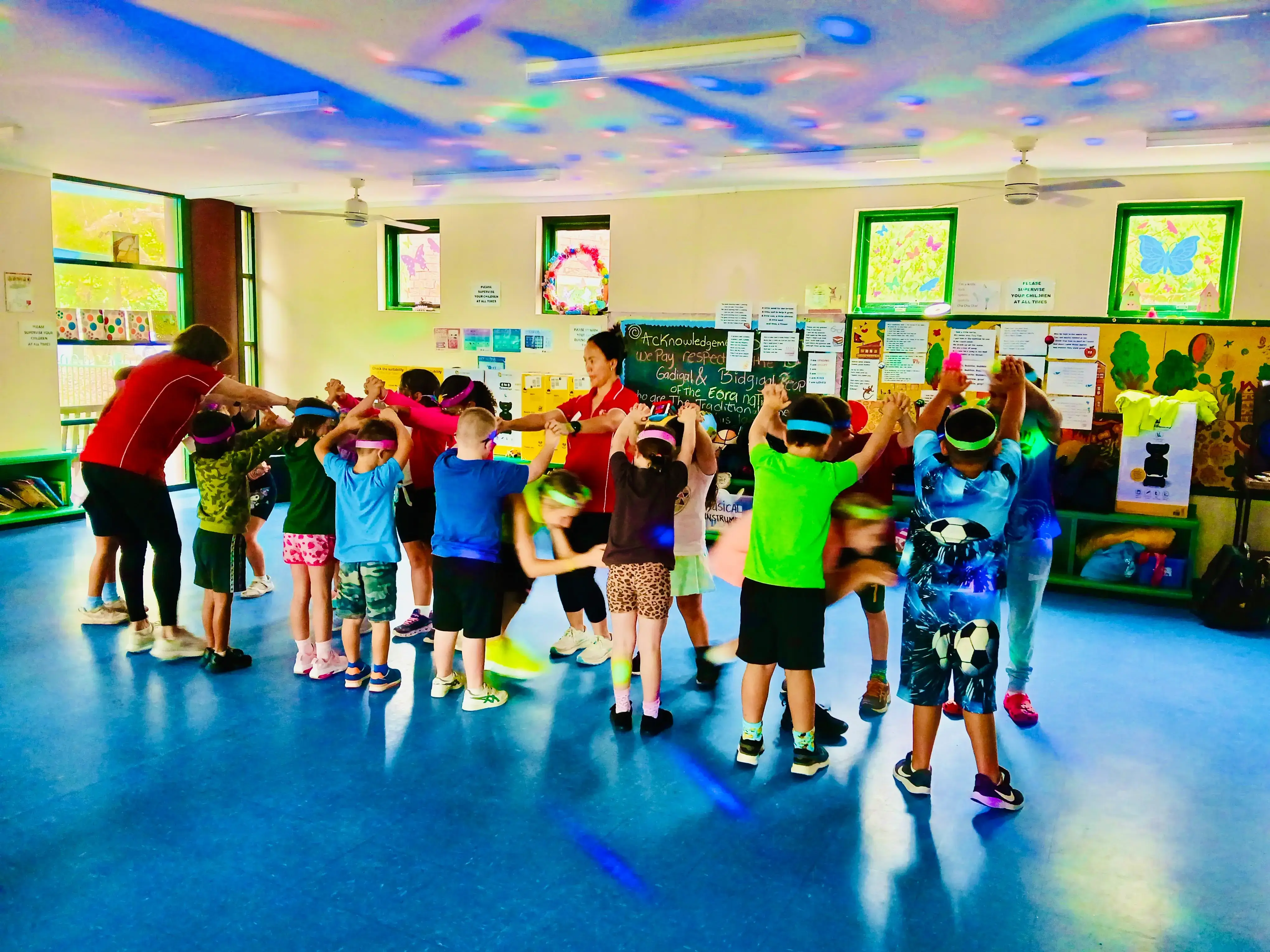 Children in headbands dancing in a vacation care hall under coloured disco lights