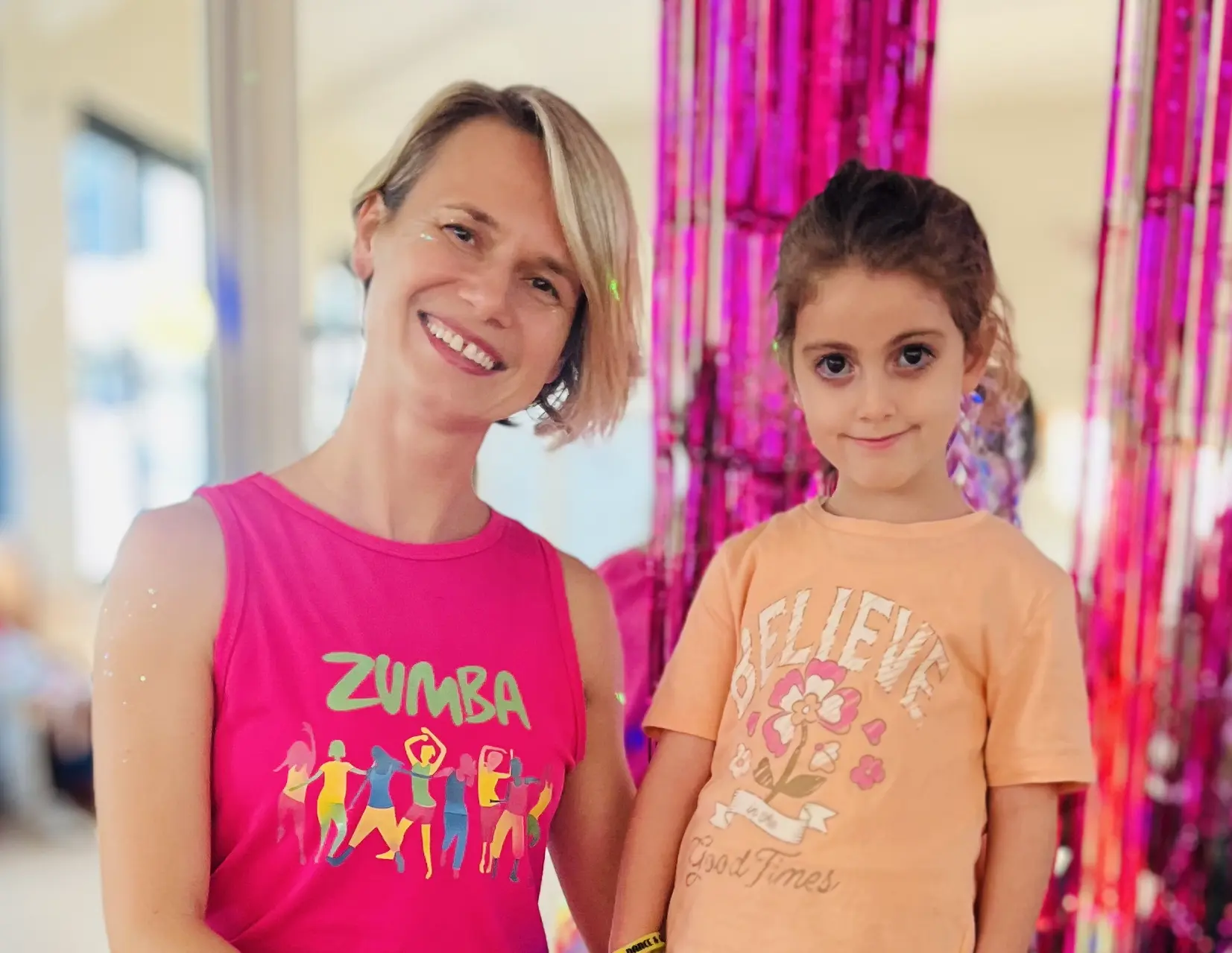 Elena and the birthday girl smiling together in front of party streamers